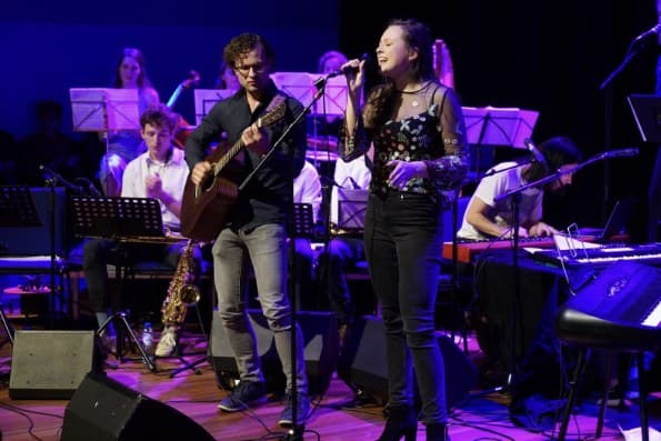 Singer and guitarist performing with a band behind them